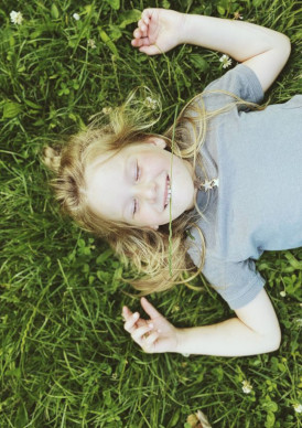 benedicts-law Child lying on her back in a field of grass & flowers